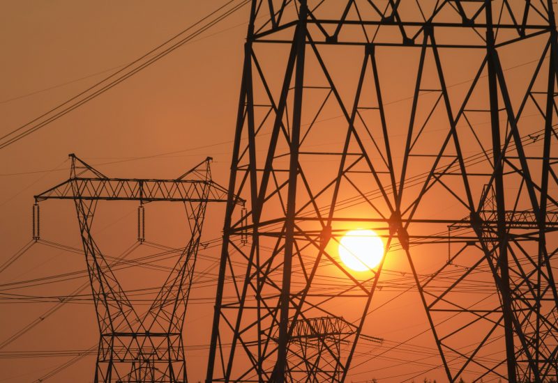 Electricity pylon and power lines with sun behind.